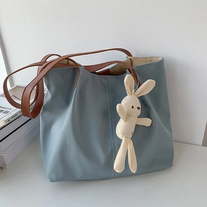 Detail of light blue nylon tote bag with brown leather straps and bunny charm accessory