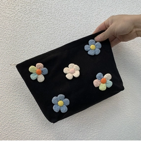 Detail of a black canvas cosmetic bag with 3D fabric flowers and a metal zipper