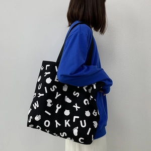 Detail of a black canvas tote bag with white graphic prints worn by a model