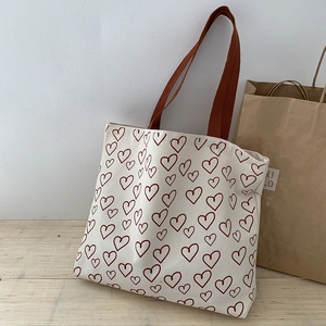 Detail of cream canvas tote bag with red heart patterns on a wooden tabletop