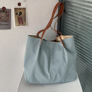 Detail of light blue nylon tote bag with brown handles in soft sunlight