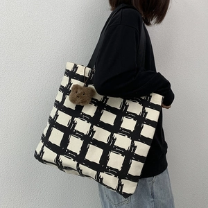 Detail of checkered canvas tote bag with shoulder strap and a cute plush bear charm