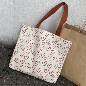 Close-up of durable canvas tote with red heart print and brown woven shoulder strap