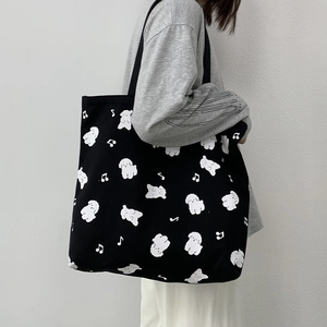 Modèle portant un grand sac cabas en toile noire avec motifs caniches et notes de musique
