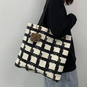 Detail of large canvas tote bag with black grid pattern and bear plush charm