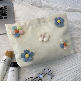 Detail of canvas makeup bag featuring five colorful 3D flower appliqués and textured surface