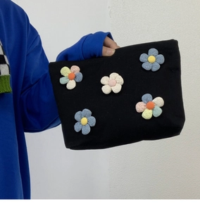 Detail of black canvas makeup bag with 3D rainbow plush flowers held by a model