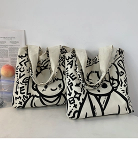 Detail of two off-white canvas tote bags with black modern graffiti art on a white desk