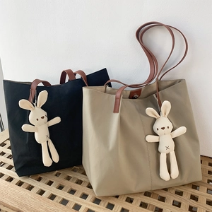 Detail view of nylon tote bags with leather straps and plush bunny charms on a wooden bench