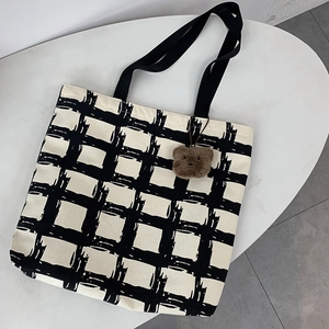 Detail of checkered canvas tote bag with black handles and a brown plush bear charm