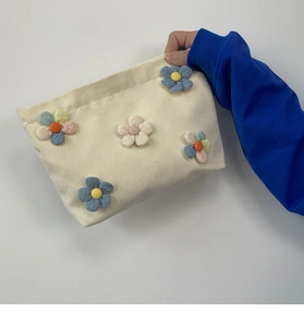 Detail of off-white canvas pouch featuring colorful 3D fabric flower decorations