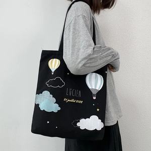Large black canvas tote bag with colorful hot air balloon print shown on a model