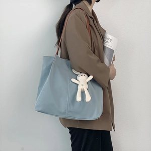 Detail of light blue nylon tote bag with plush rabbit charm and brown leather straps