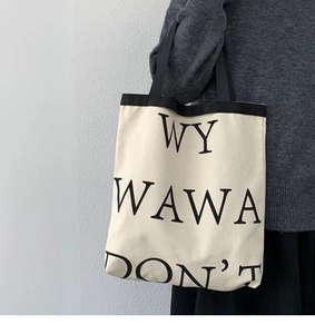 Detail of minimalist canvas tote bag with black letter print carried by a model