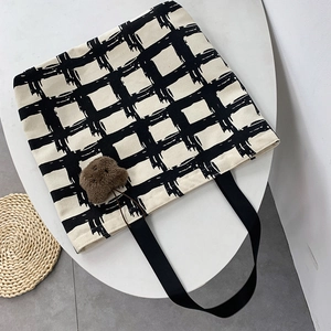Close-up of white grid canvas tote bag with black straps and cute brown bear plush charm