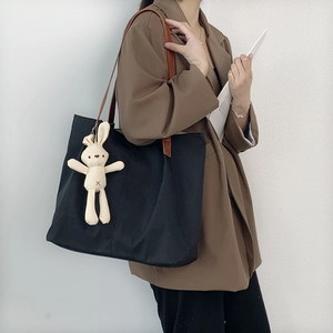 Detail of black canvas tote bag with leather straps and cute bunny charm accessory