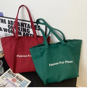 Détail de grands sacs cabas en toile rouge et verte avec lettres Famous For Pizza