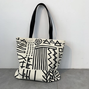 Close-up of cream canvas tote bag with black tribal abstract patterns and shoulder straps