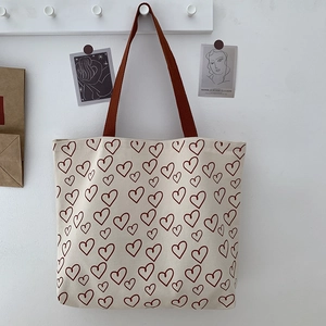 Detail of canvas tote bag featuring red heart patterns and a brown shoulder strap