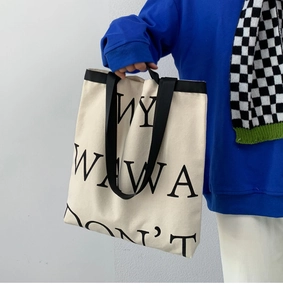 Close-up of a large canvas tote bag with black lettering and contrasting shoulder straps
