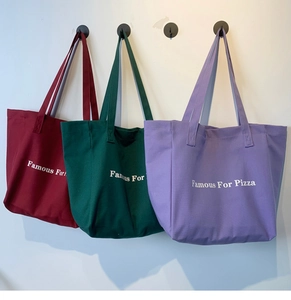 Détail de grands sacs cabas en toile en couleurs bordeaux, vert foncé et lavande