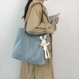 Detail view of Morandi blue nylon tote bag with brown strap and plush rabbit charm