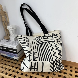 Artistic cream canvas tote bag with black tribal graffiti on a stylish wooden bench
