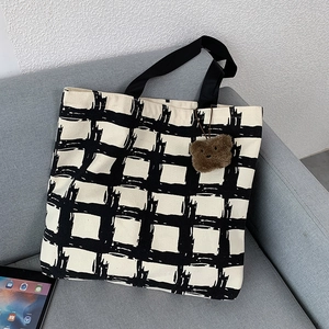 Close-up of black and white checkered canvas tote bag with a brown teddy bear charm detail