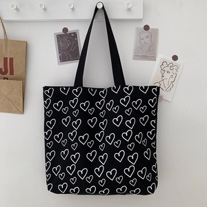 Detail of black canvas tote bag featuring white heart patterns and dual shoulder straps