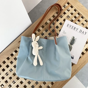 Detail of light blue canvas tote bag with brown leather handles and a plush rabbit charm