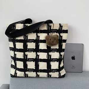 Detail view of large canvas tote bag with black and white checkered pattern and bear charm
