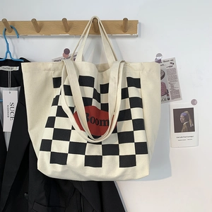 Detail of checkered canvas tote bag with red Boom print hanging on a wooden hook