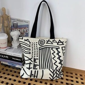 Detail of a large canvas tote bag with black geometric art on a wooden bench