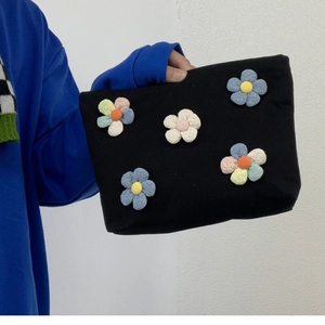 Portable black canvas makeup bag with five colorful 3D floral appliques in hand
