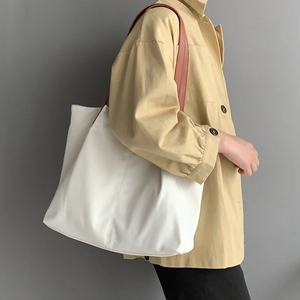 Minimalist white nylon tote bag with brown leather straps worn on a beige jacket