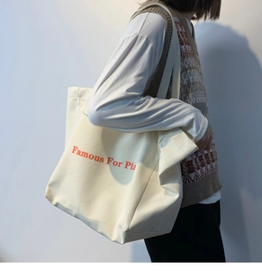 Détail du sac cabas en toile crème avec imprimé orange Famous For Pizza sur modèle