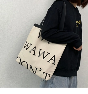 Detail of large canvas tote bag with WAWA DON'T lettering on shoulder model