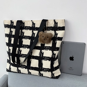Close-up of canvas tote bag with black and white grid pattern and plush bear charm detail
