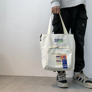 Detail der weißen Nylon-Tragetasche mit orangefarbenen und lila Reise-Stoffetiketten