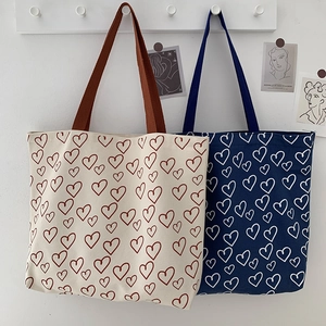 Detail view of two canvas tote bags with heart prints in beige and navy on a wall