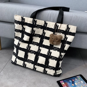 Detail of checkered canvas tote bag with black strap and cute brown plush bear charm
