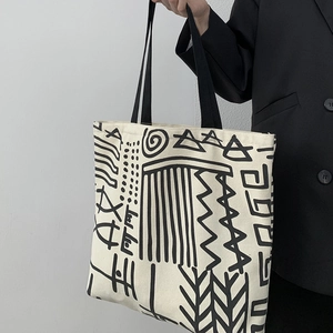 Close-up of cream canvas tote bag featuring black abstract tribal graphics and straps