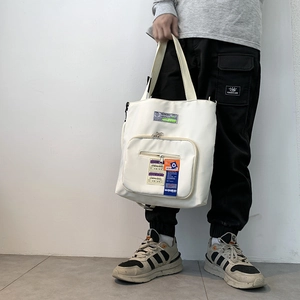 Tragebild einer weißen Canvas-Tragetasche mit funktionaler Reißverschlusstasche und Utility-Labels