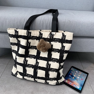 Detail of checkered canvas tote bag with brown plush bear charm and spacious interior
