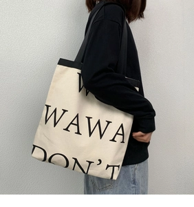Detail of a beige canvas tote bag featuring black WAWA DON'T lettering on the front side