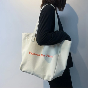 Détail d'un sac fourre-tout en toile avec imprimé Famous For Pizza rouge et large bandoulière