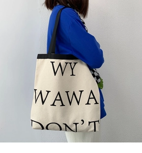 Detail of canvas tote bag with WY WAWA letters and black contrast straps on white