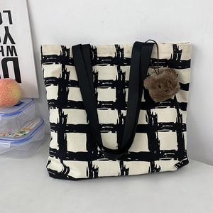 Detail of canvas tote bag with black grid pattern and brown plush bear charm