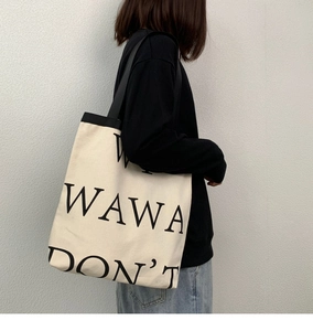 Detail of minimalist canvas tote bag with WAWA DON'T lettering and black shoulder strap