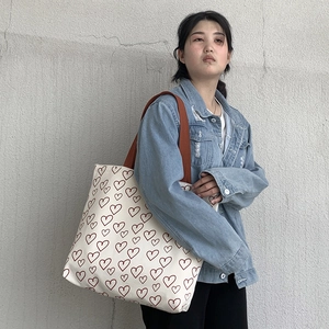 Detailed view of canvas tote bag with red heart pattern and brown woven straps